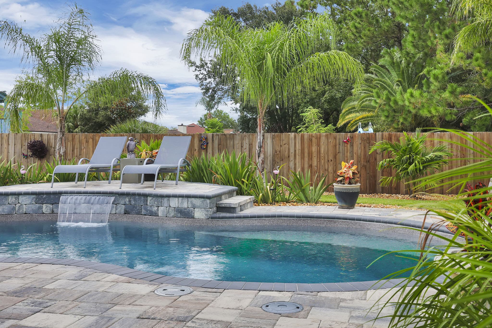 "Pool with lounge chairs on a raised platform with palm trees surrounding it"