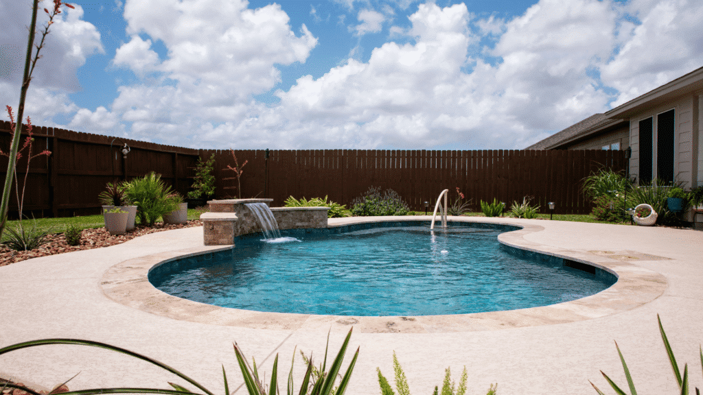 Freeform inground pool with stone waterfall feature and travertine decking in a Corpus Christi backyard"