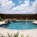 Freeform inground pool with stone waterfall feature and travertine decking in a Corpus Christi backyard"