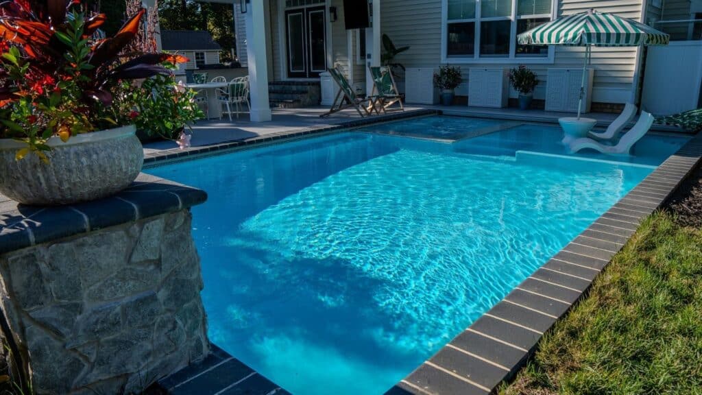 "Rectangular pool with sun shelf, striped umbrella, lounge chairs, and stone planter pillar"