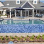 "Backyard pool with blue mosaic tile wall, raised spa, lounge chairs, and a covered porch behind"