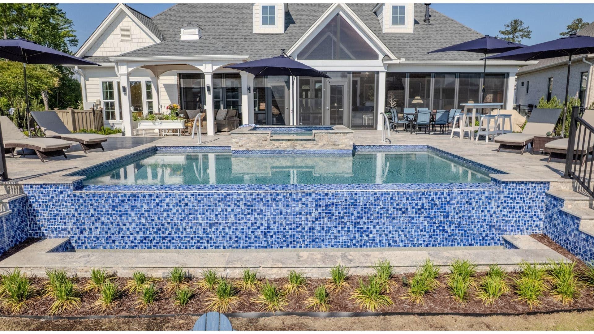 "Backyard pool with blue mosaic tile wall, raised spa, lounge chairs, and a covered porch behind"