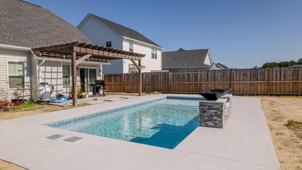 "Rectangular inground pool with raised stone feature, concrete deck, and pergola by a fenced yard"