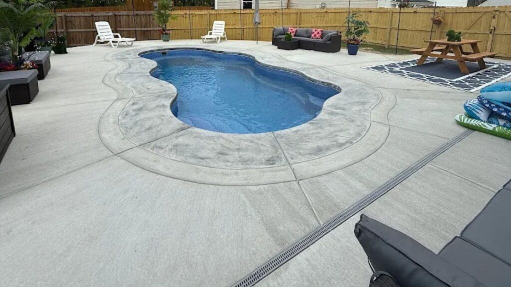 "Freeform inground pool with stamped concrete coping, deck drain, lounge chairs, and picnic table"