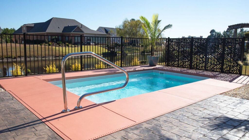 "Small inground pool with steel handrail, terracotta-colored coping, black fence, and stamped patio"