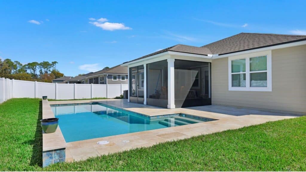 "Rectangular pool in a Jacksonville backyard with a sun shelf and entry steps, travertine deck and coping, a raised tiled wall with planters, and a screened sun room beside a white vinyl fence"