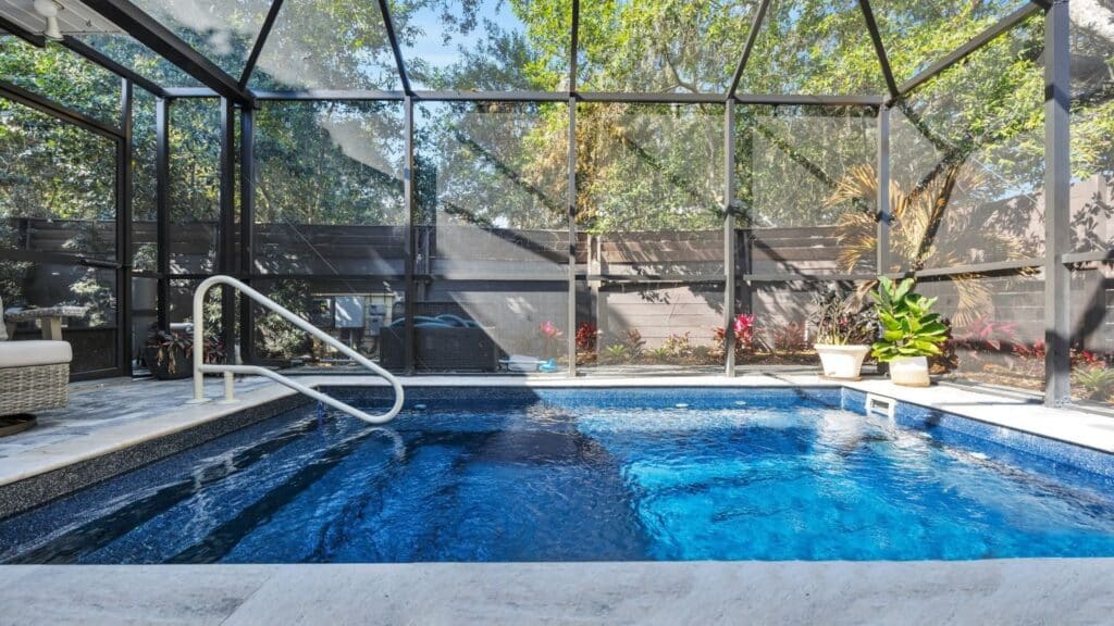 Screened-in inground pool with deep blue water, a white handrail, and potted plants along the fence