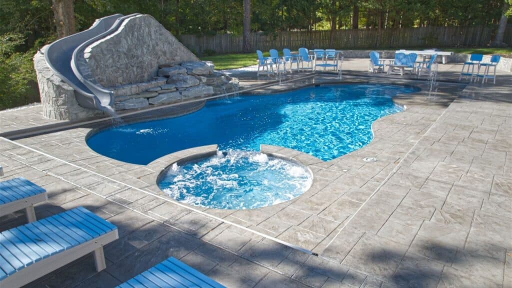 "Inground pool with attached spa, rock waterfall slide, and stamped concrete patio"